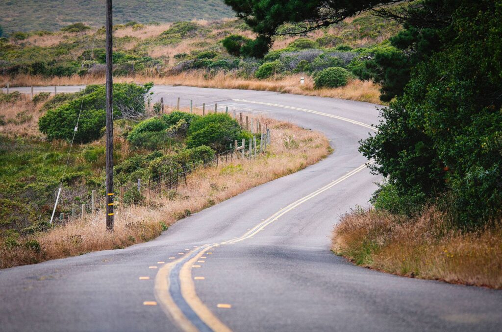 Quiet two-lane rural road winding through dry grass and coastal scrub hills in soft daylight, representing an SR-67 crash claims guide without showing a collision.