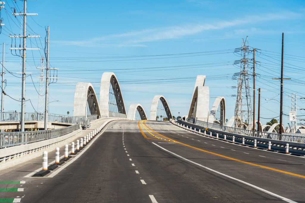 Empty city bridge roadway with white arches under a clear blue sky, representing a guide to driverless car crash claims in California without showing a crash or any vehicle brand.